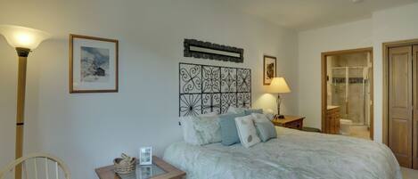Quarto com uma cama grande, mesa de cabeceira com abajur, uma cadeira e um quadro na parede.