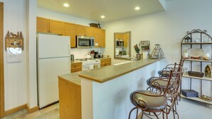 Una cocina con armarios de madera, un refrigerador, un microondas, una estufa y una zona de bar con taburetes.