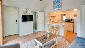 A spacious living area with a wooden coffee table, a TV, and a kitchen with a bar. - Tropical Island Escape w/ Deck, Walk to Avalon Bay (Avalon)
