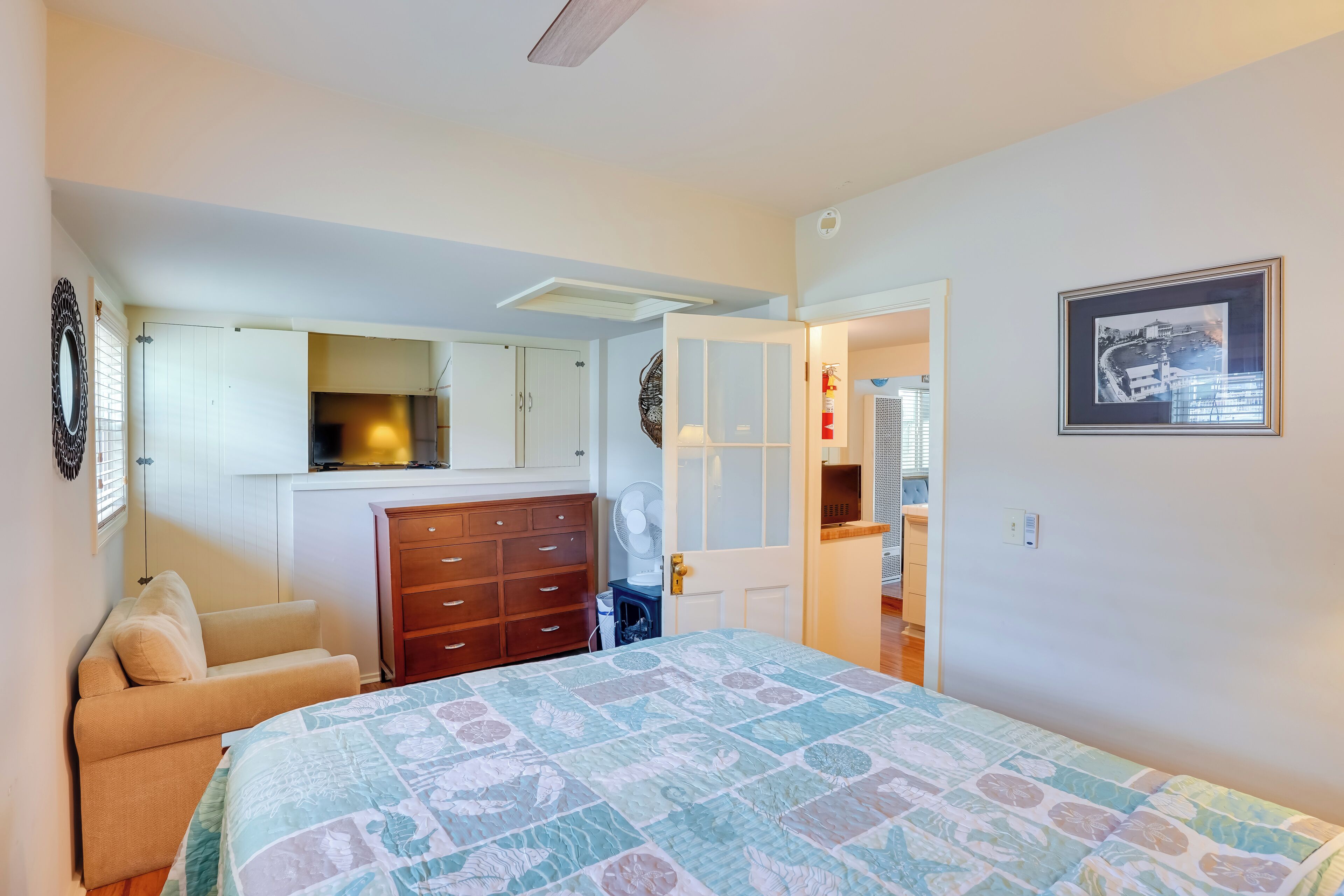 Un dormitorio con cama, cómoda, silla y puerta que da a otra habitación.