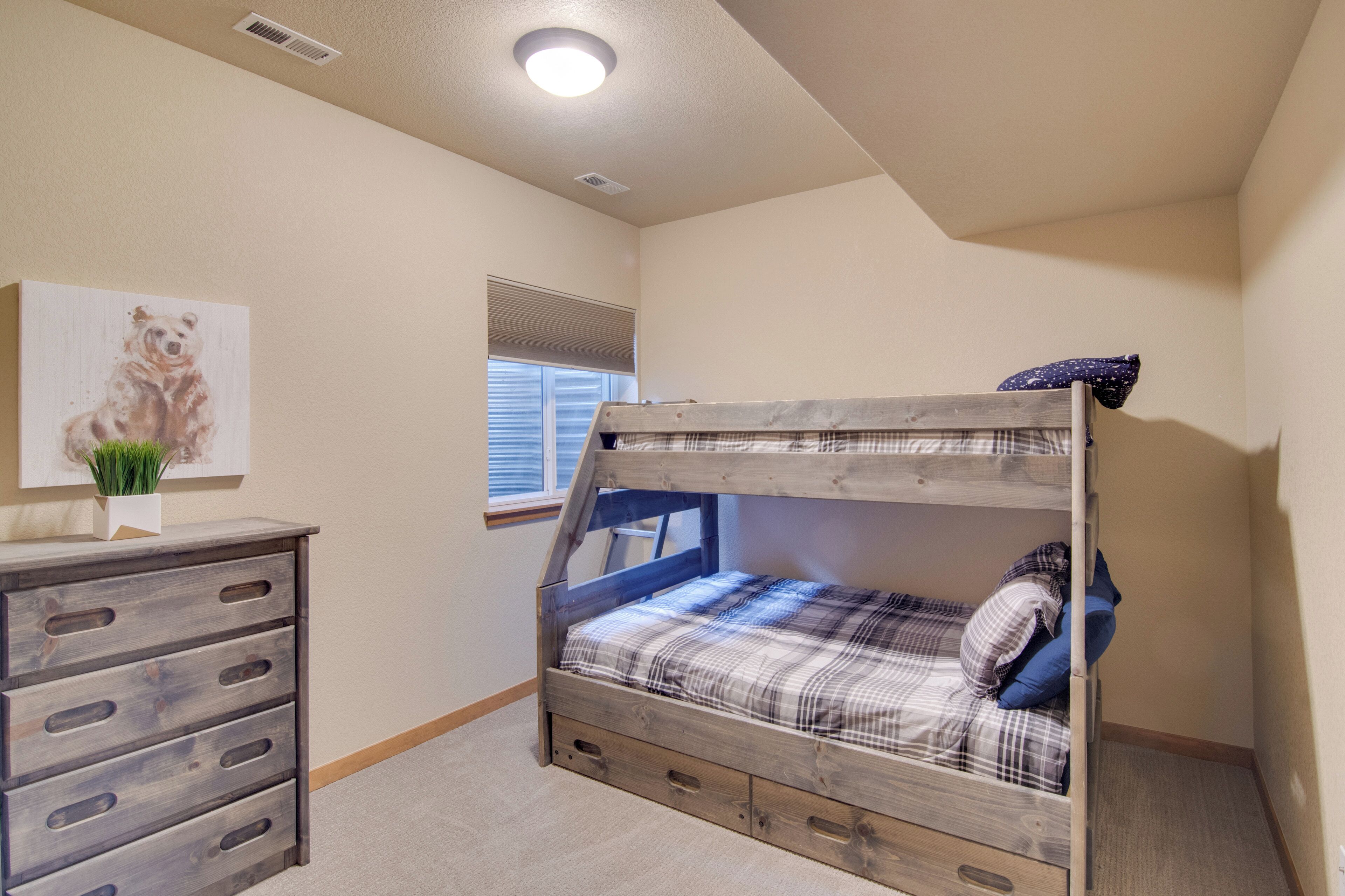 Une chambre avec un lit superposé, une commode, une fenêtre avec des stores et un tableau accroché au mur.