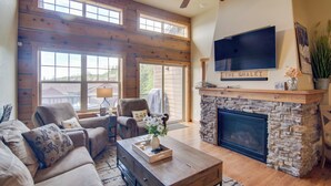 A spacious living room with a stone fireplace, a large TV mounted above it, and a ceiling fan. - Winter Park Chalet w/ Hot Tub + Free Shuttle! (Fraser)