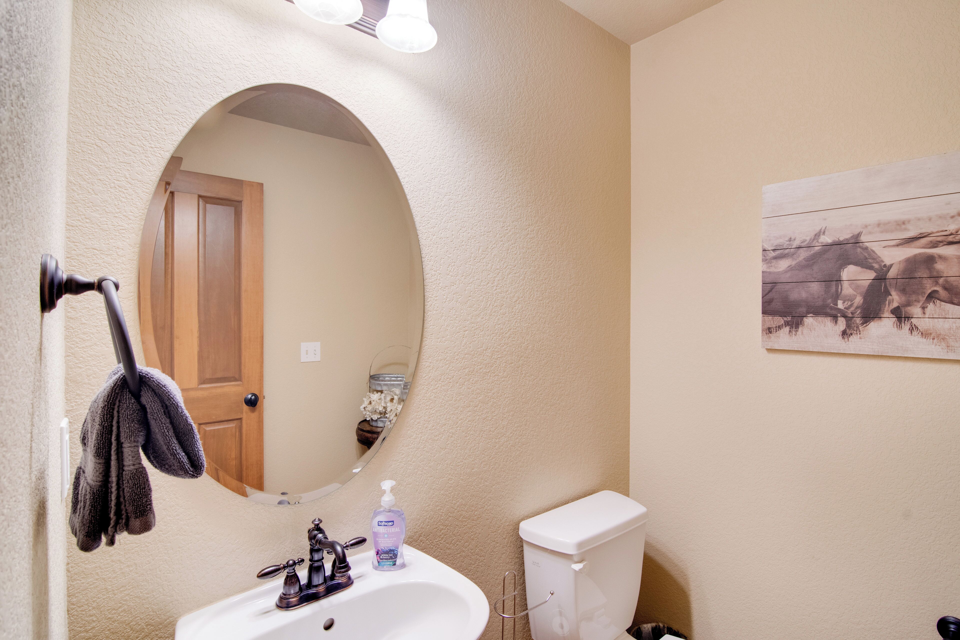 A bathroom with a white sink, a mirror, a towel rack, a toilet, and a wall-mounted painting.