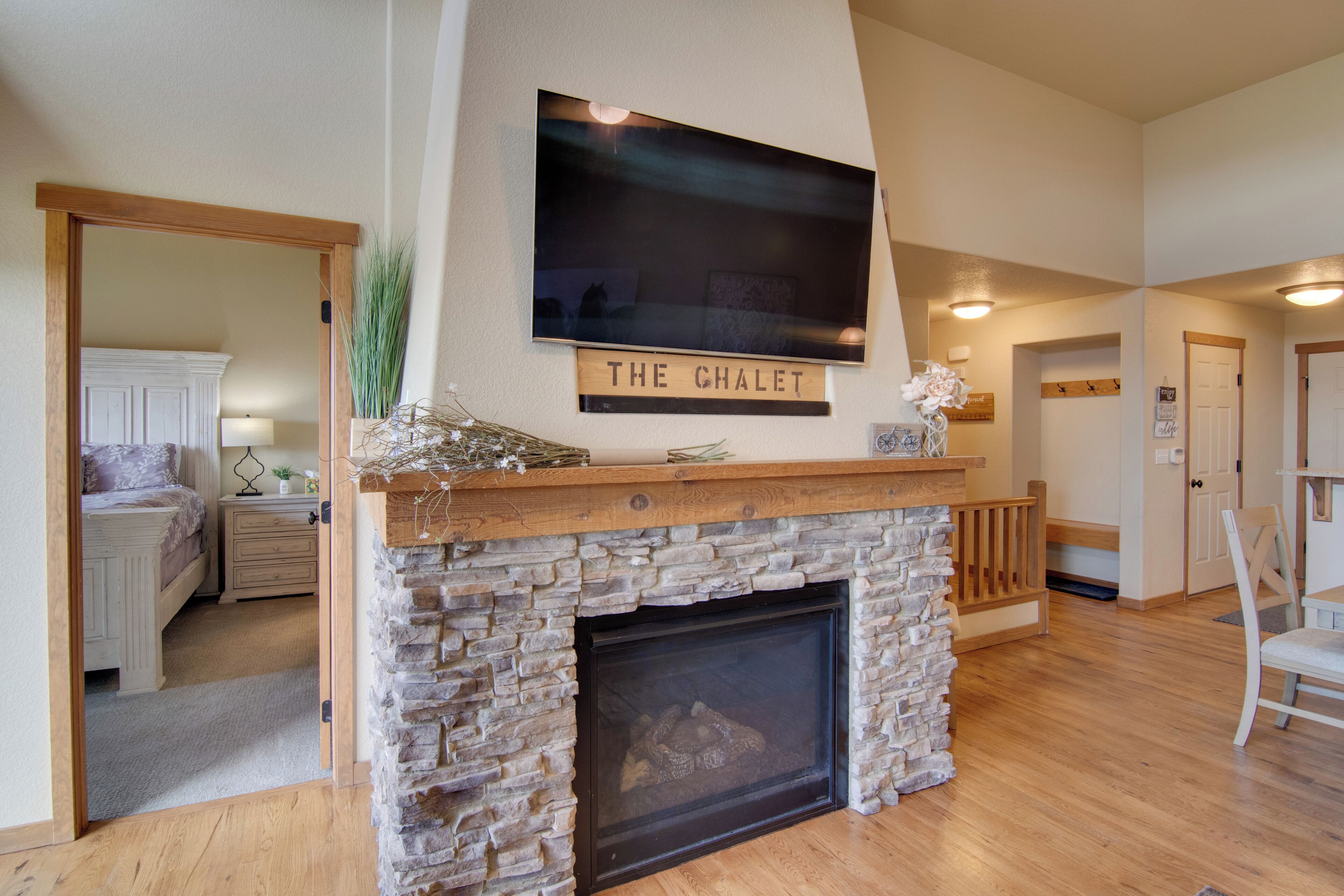 A living room with a stone fireplace, a mounted flat-screen TV above it, and a sign reading "THE CHALET".