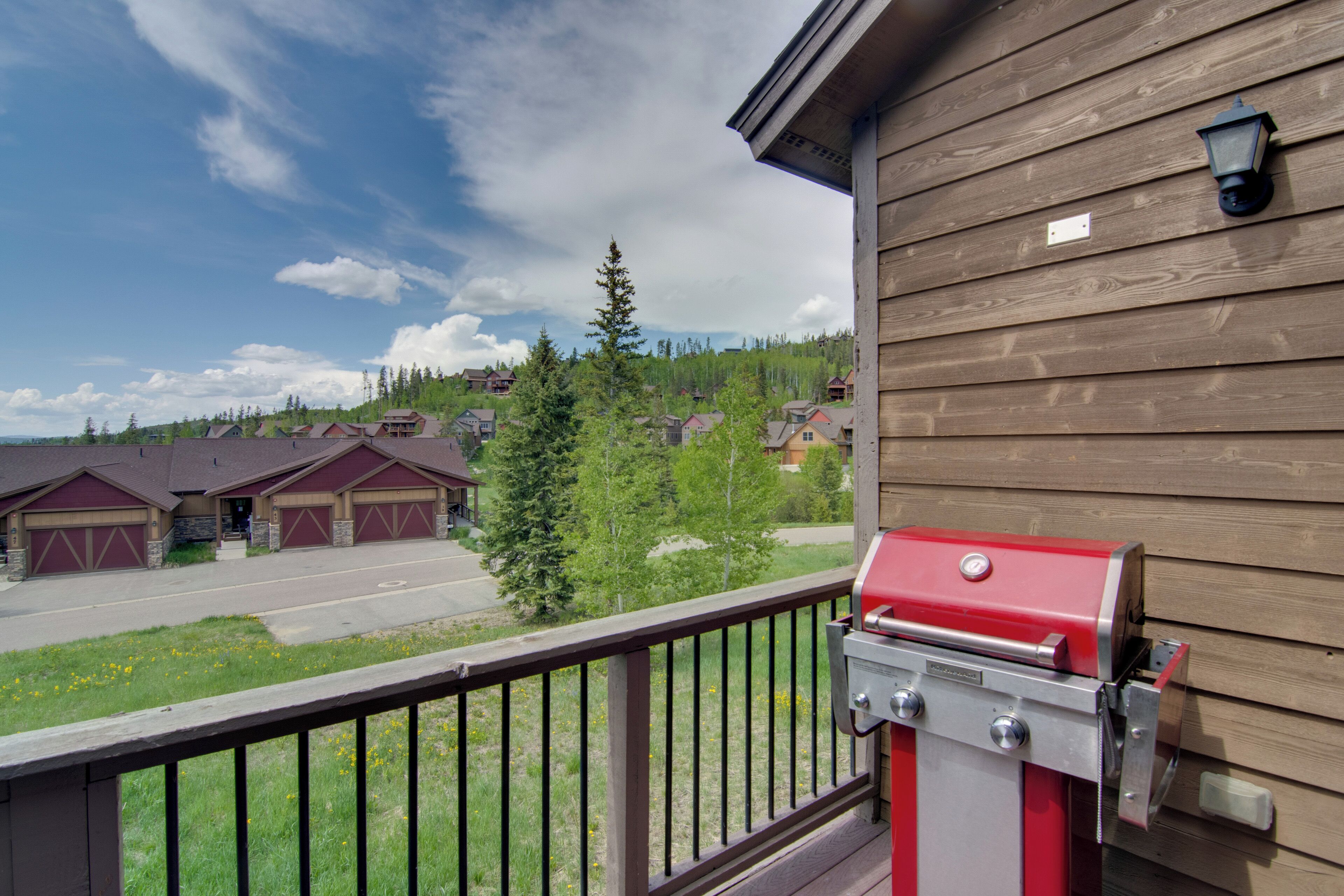 A wooden building with a barbecue grill on the deck, a view of houses and trees in the background.