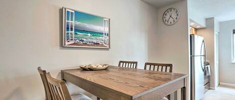 A dining area with a wooden table and chairs, a clock on the wall, and a kitchen in the background.
