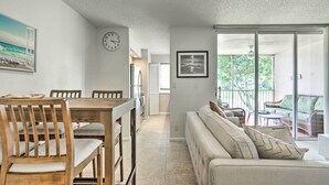 A modern living room with a wooden dining table, beige sofa, and a balcony with wicker furniture. - Jupiter Bay Condo w/ Pool < Half Mile to Beach! (Jupiter)