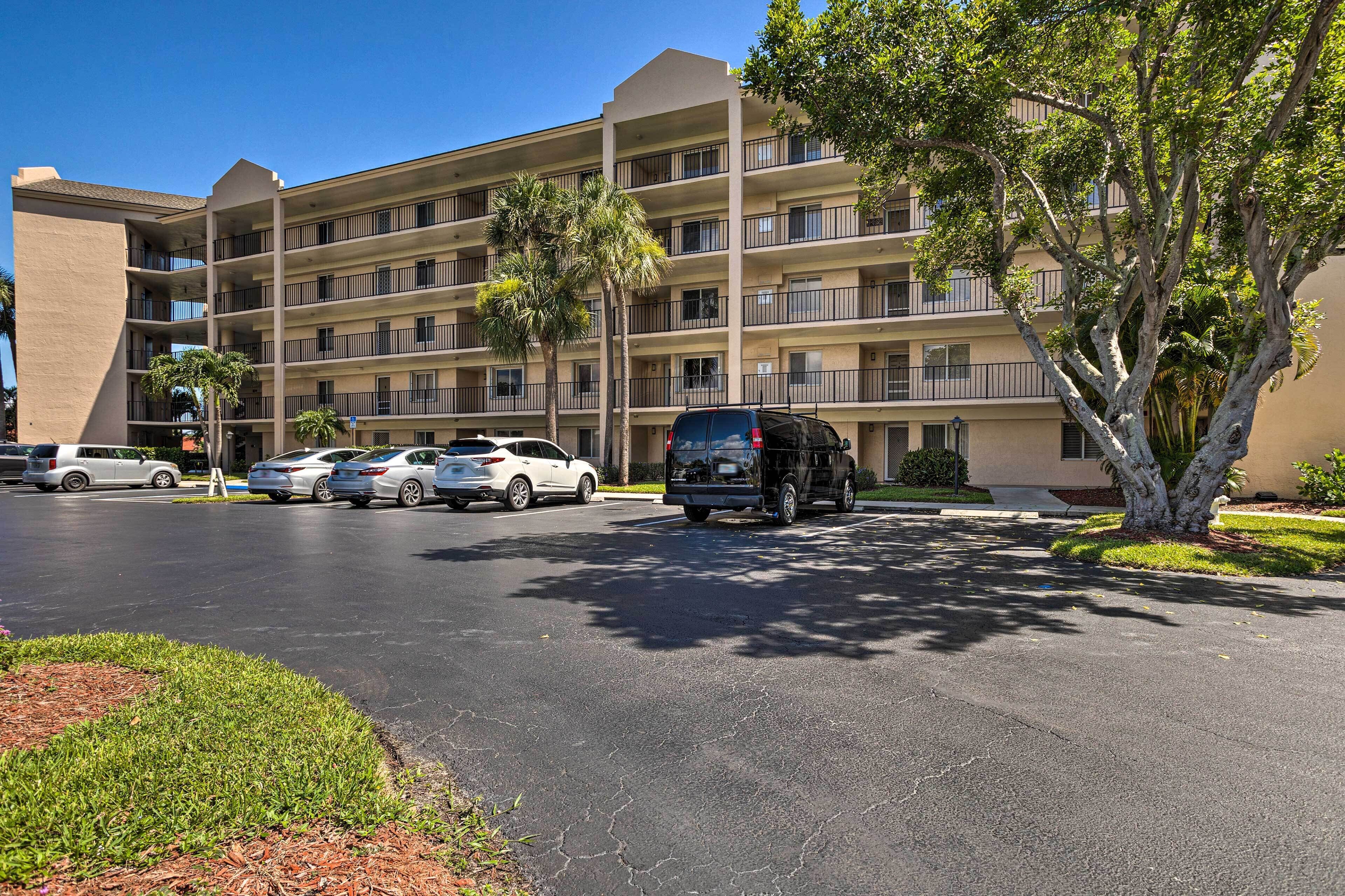 A multi-story hotel with a parking lot, several cars, and palm trees.