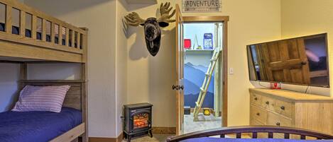 A bedroom with a bunk bed, a fireplace, a television, and a door leading to a mountain view.