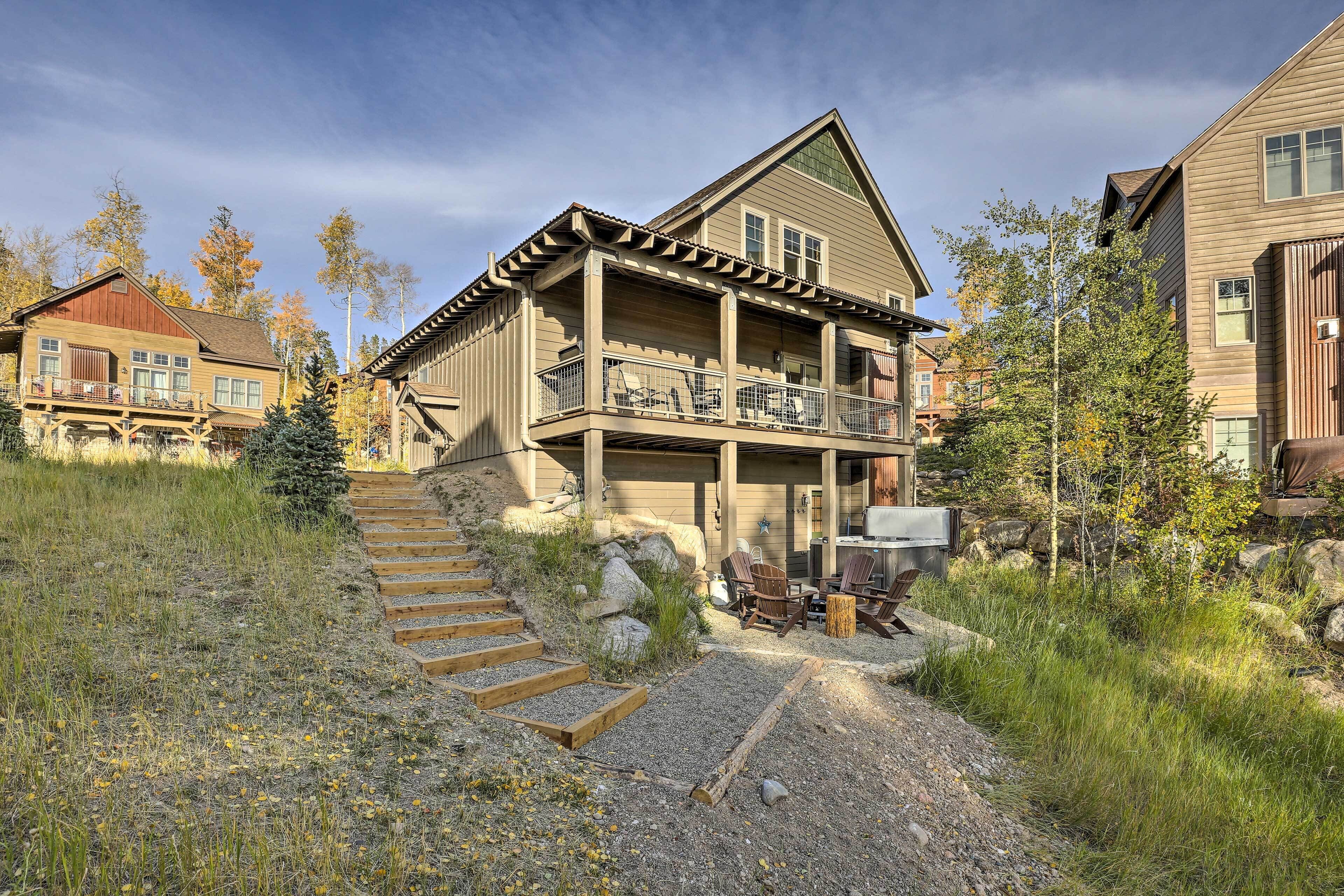 A two-story house with a balcony, a wooden staircase leading to the entrance, and outdoor seating.