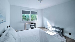 Une chambre à coucher avec un lit, un bureau, une chaise, une fenêtre et une porte.