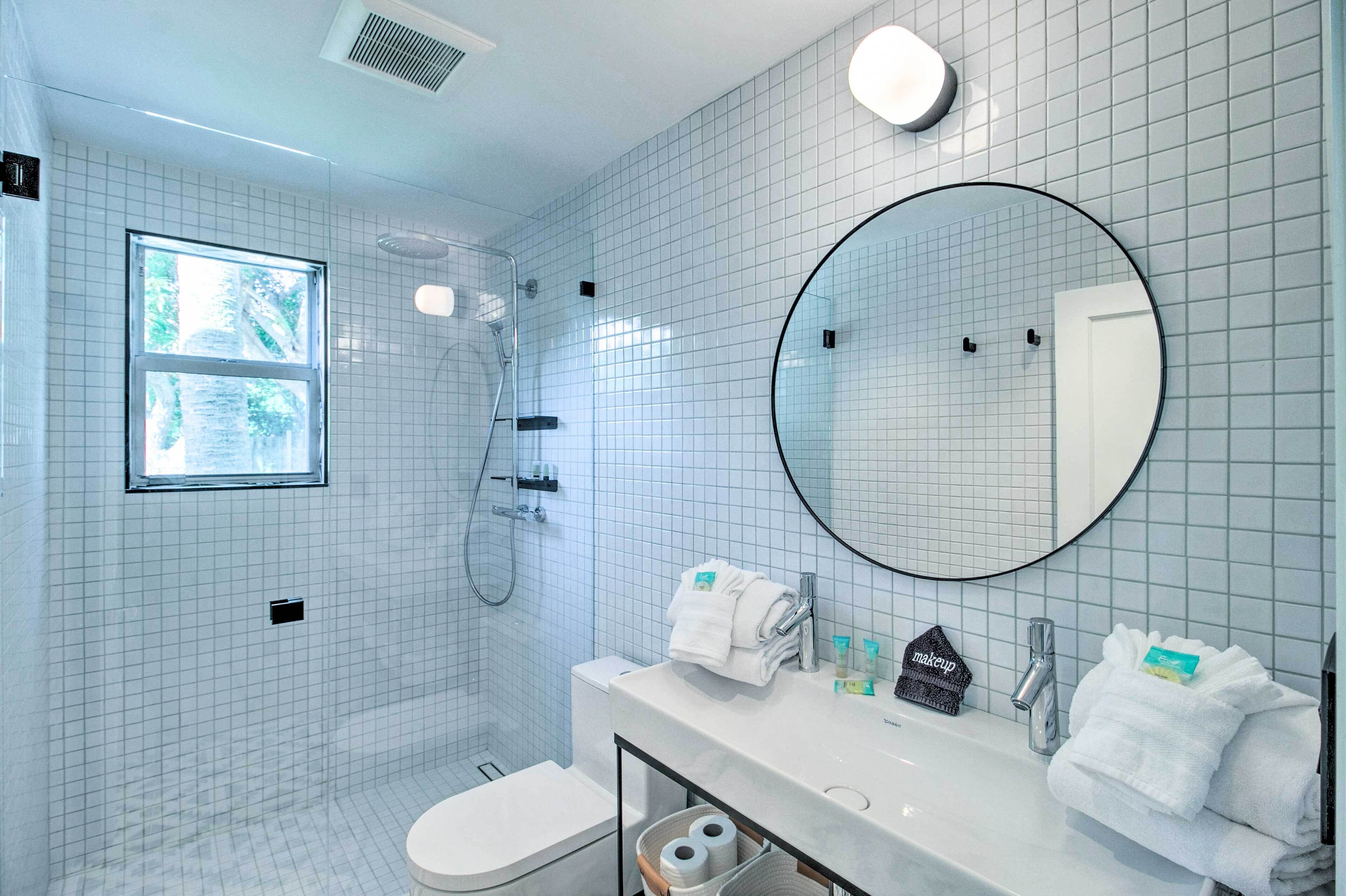 Un baño moderno con ducha, inodoro y lavamanos, que cuenta con un espejo grande y una ventana.