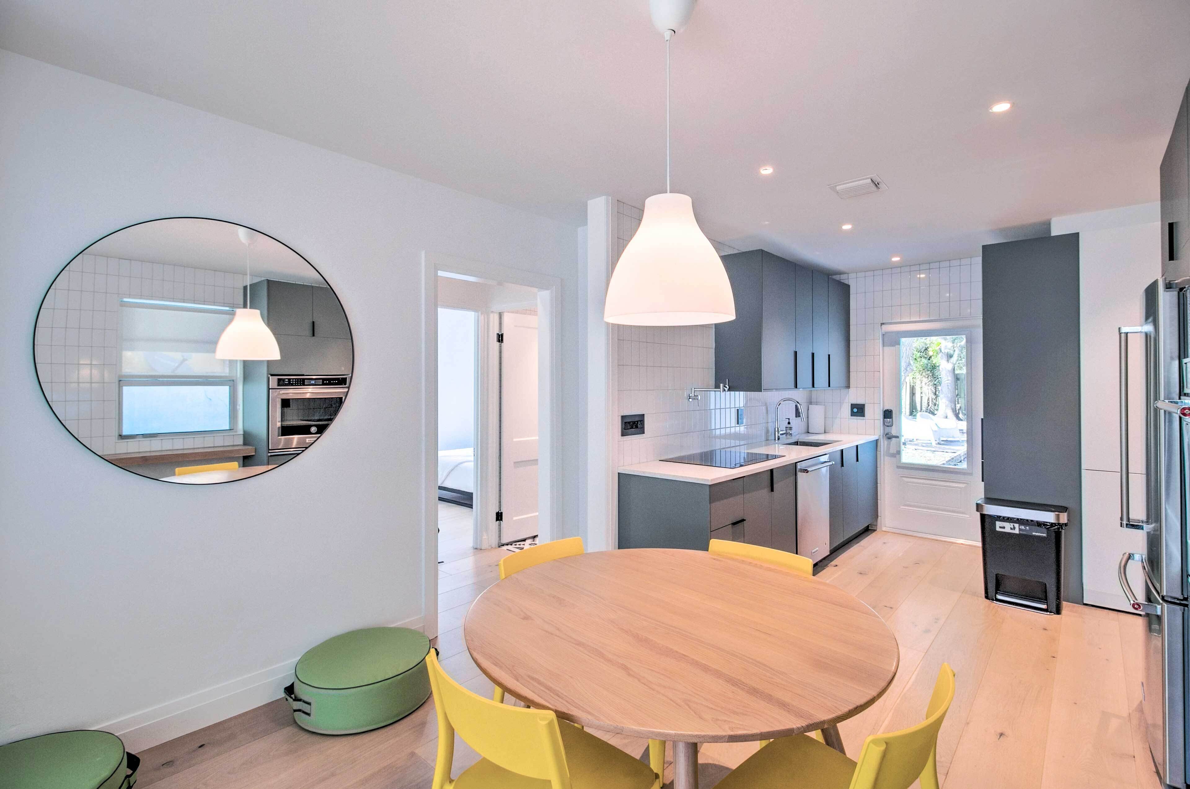 Una cocina moderna con una isla central, una mesa redonda con sillas amarillas y un espejo grande en la pared.