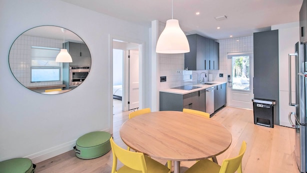 Une cuisine moderne avec un îlot central, une table de salle à manger ronde entourée de chaises jaunes et un grand miroir au mur.