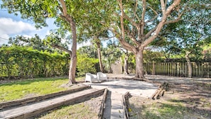Un jardin avec une terrasse en béton, deux chaises blanches et une clôture en bois.