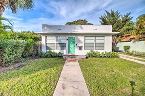 A modern two-story house with a green door, a concrete pathway leading to the entrance, and a well-maintained garden.