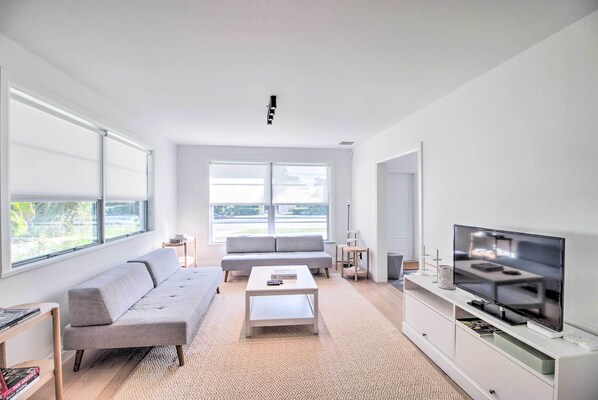 A modern living room with a sofa, coffee table, TV, and large windows.