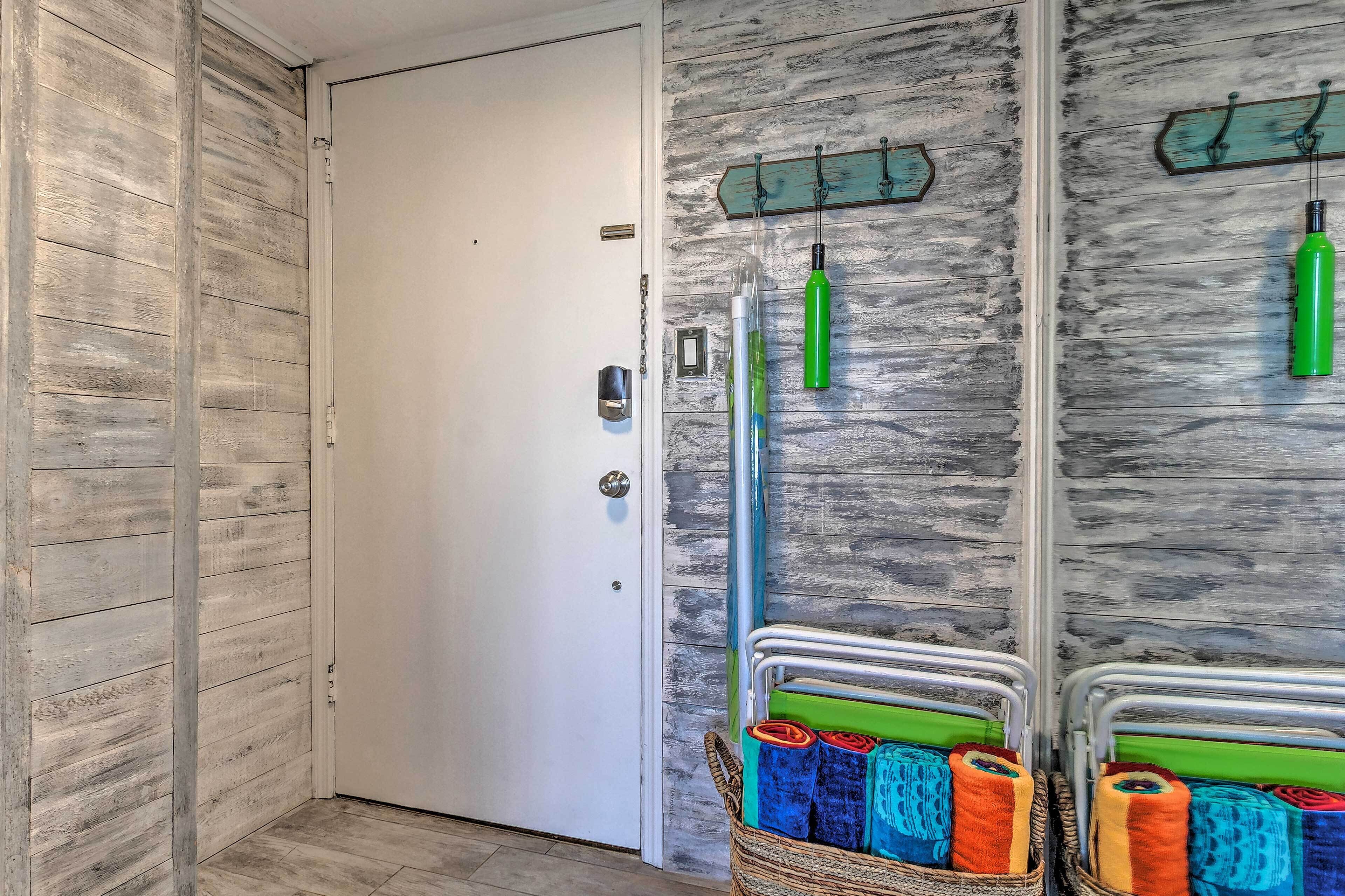 A room with a wooden wall, a white door, and a metal rack holding cleaning supplies.