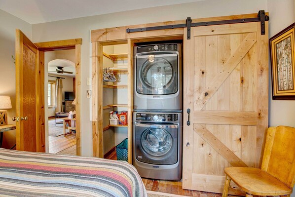 A laundry room with two stacked front-loading washers and dryers, wooden sliding doors, and a chair.