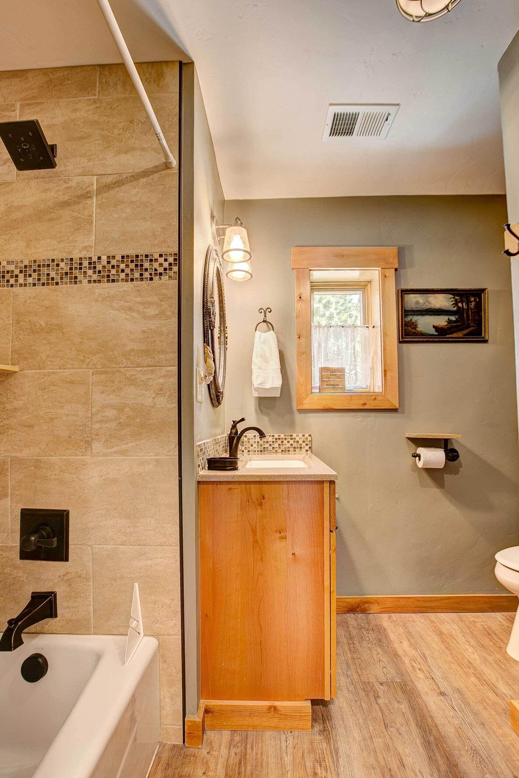 A bathroom with a bathtub, a wooden vanity, a mirror, a window, and a toilet.