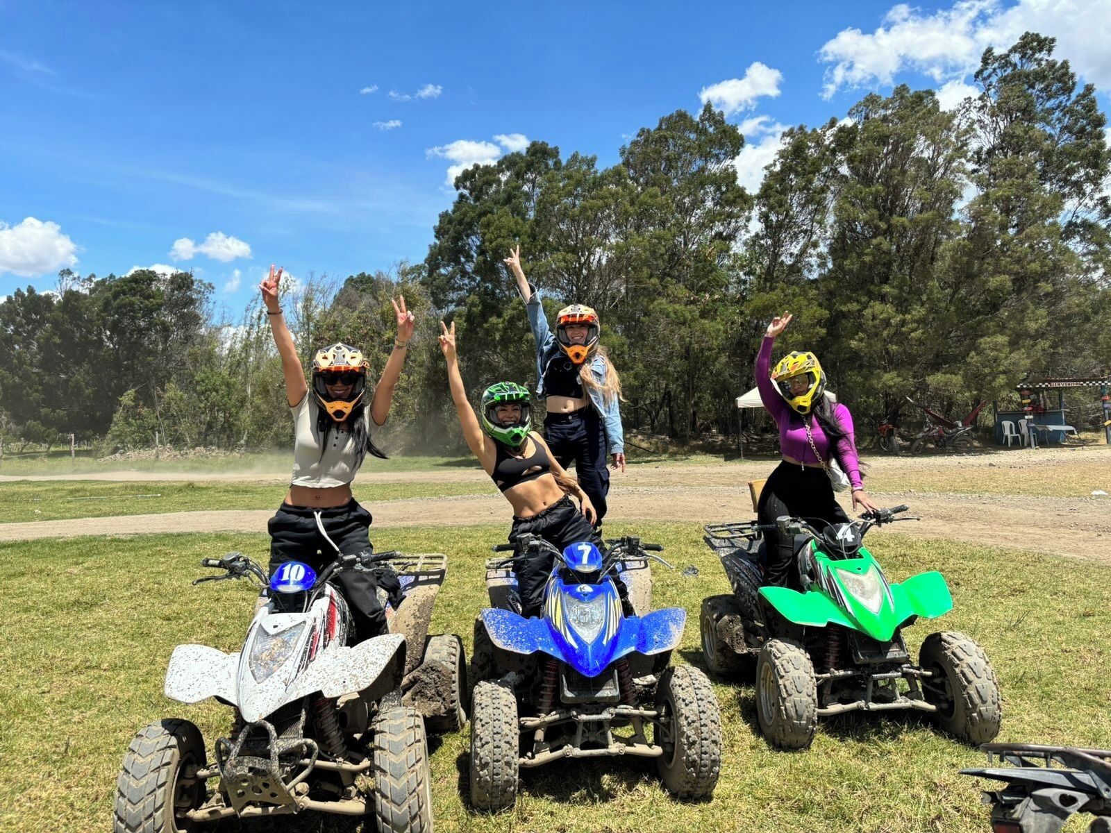 Three people on ATVs in a grassy field with trees in the background.