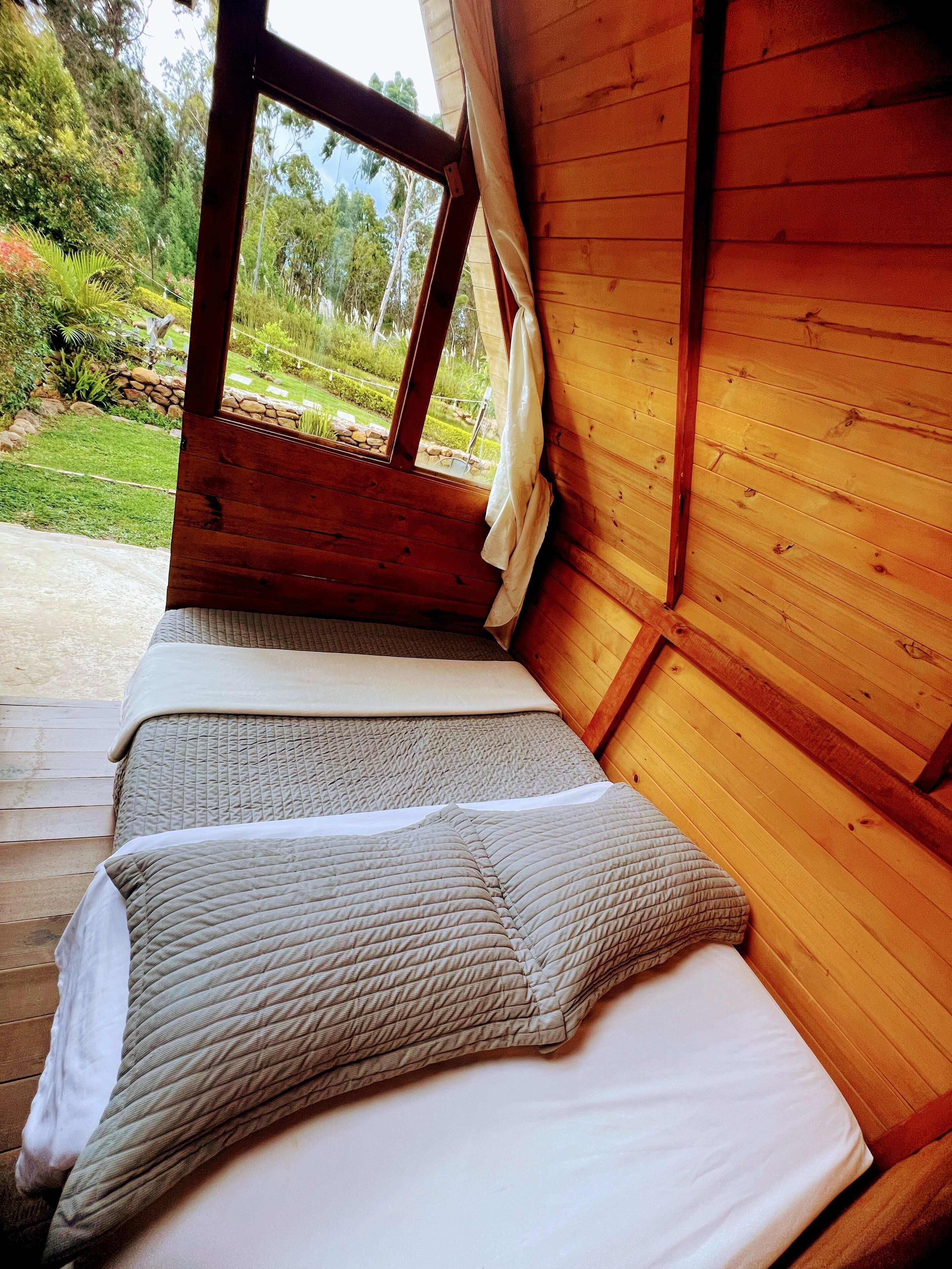 A wooden cabin with a bed and a window overlooking a garden.