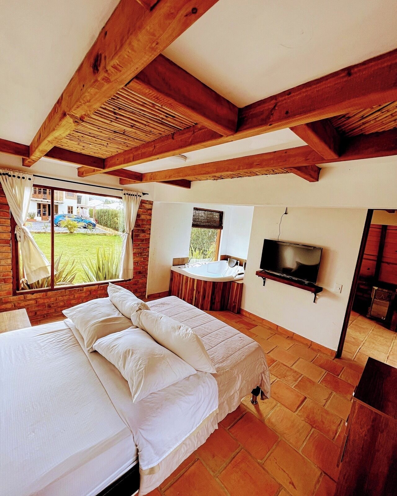 Ein Schlafzimmer mit Bett, Fernseher, Bad und Blick auf ein Haus und einen Garten.