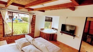Ein Schlafzimmer mit Bett, Fernseher, Bad und Blick auf ein Haus und einen Garten.