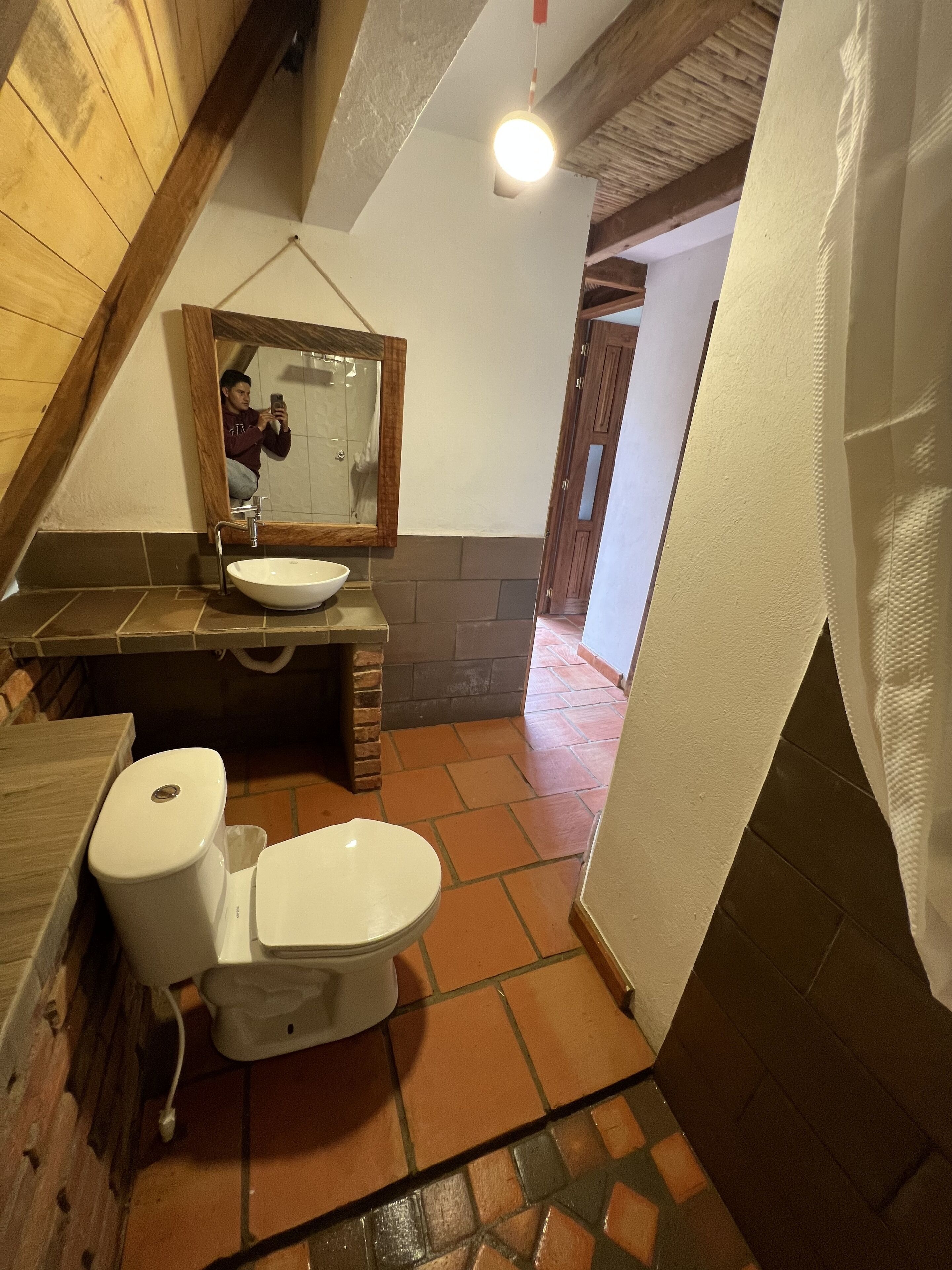 Un bagno con soffitto in legno, lavandino bianco, un water e uno specchio.