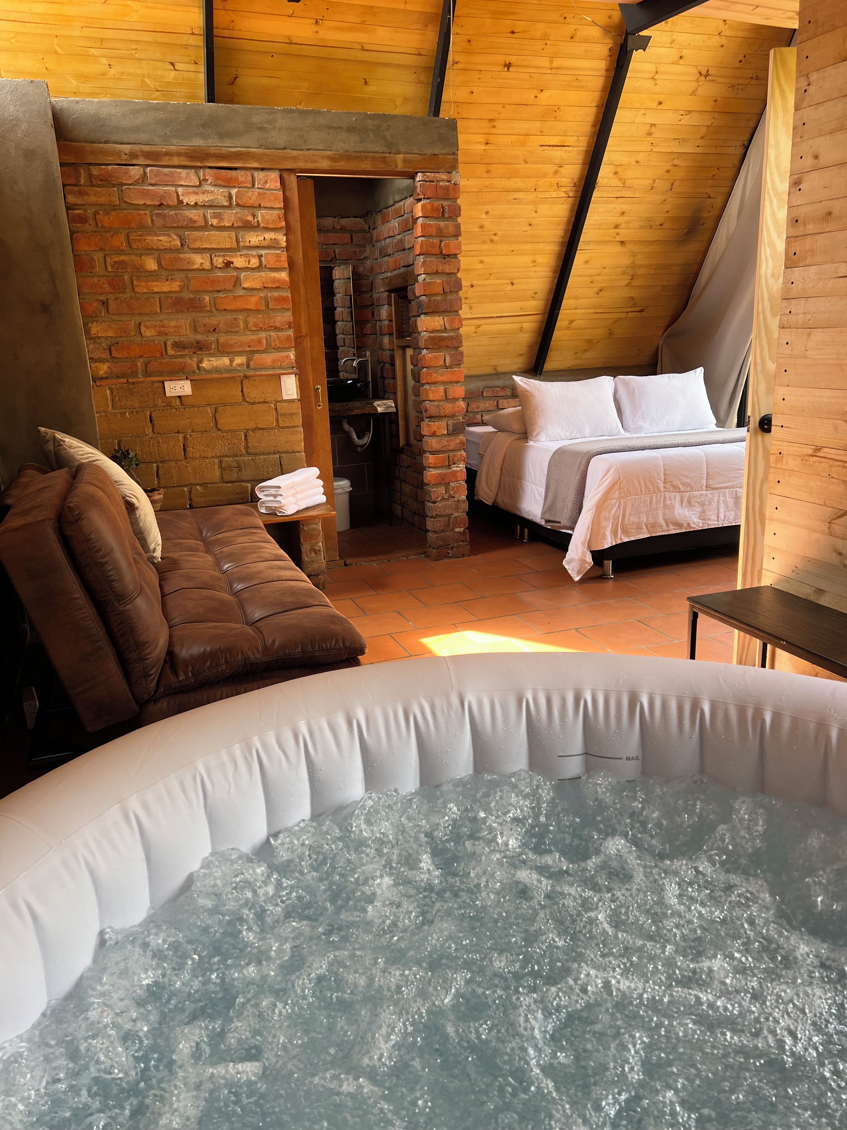 A cozy room with a brick wall, a bed, a sofa, and a hot tub.