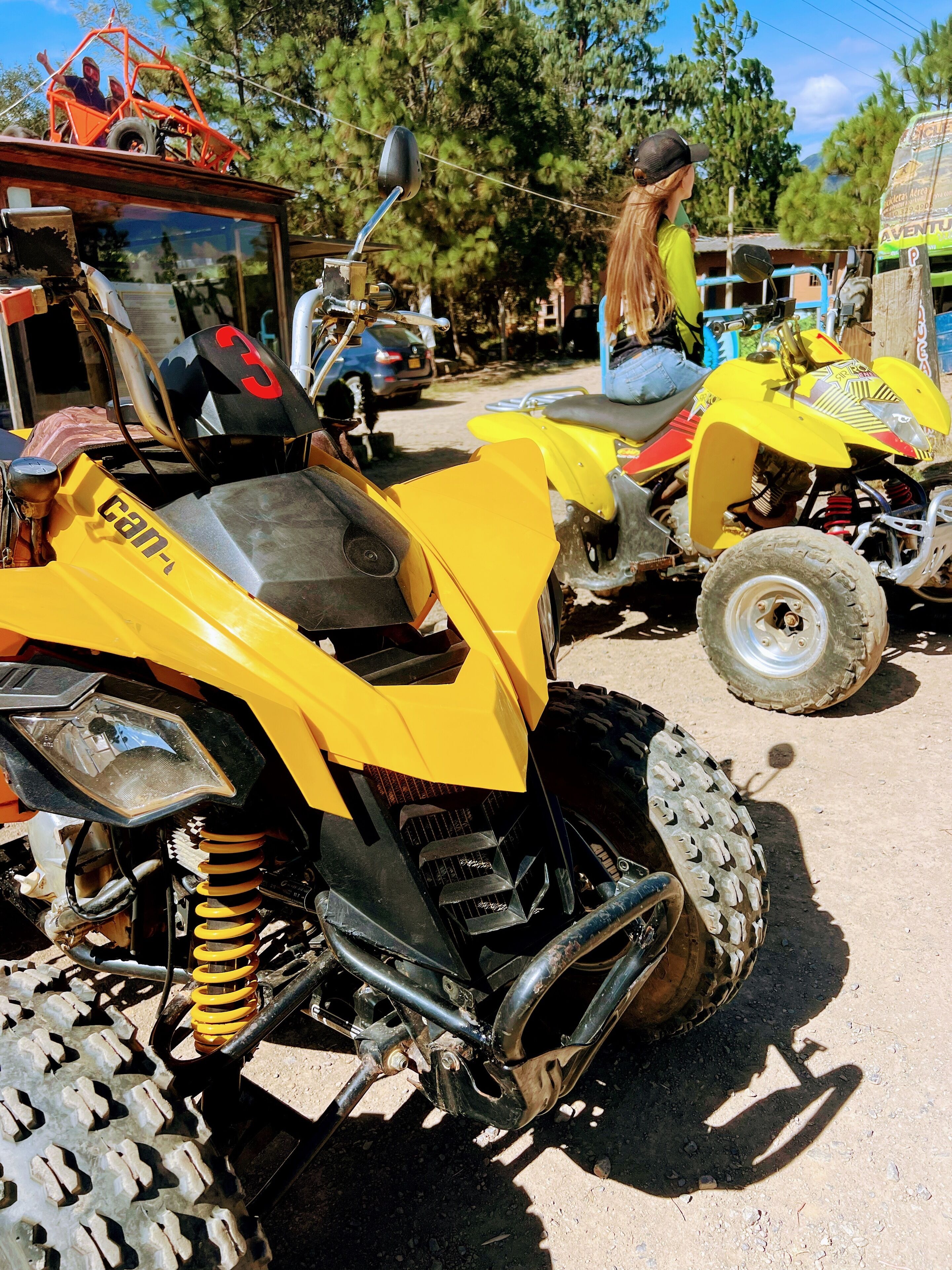Un quad jaune, dont on peut voir la suspension et les pneus, est garé sur un sol en terre.
