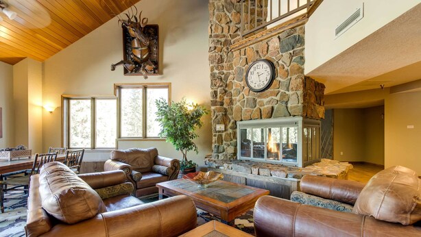 Un salón amplio con sofás de cuero, una chimenea de piedra y un comedor con mesa y sillas de madera.