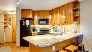 Una cocina con armarios de madera, encimera de granito, refrigerador negro, microondas, estufa y fregadero.