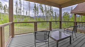 A covered outdoor deck with a table and chairs, overlooking a forested area with mountains in the background. - Fraser Retreat, Walk to Ski Shuttle & Main St (Fraser)