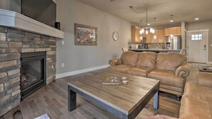 A modern living room with a stone fireplace, leather sofa, wooden coffee table, and a kitchen in the background. - Fraser Retreat, Walk to Ski Shuttle & Main St (Fraser)