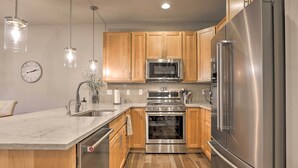 A modern kitchen with wooden cabinets, stainless steel appliances, a marble countertop, and pendant lighting. - Fraser Retreat, Walk to Ski Shuttle & Main St (Fraser)