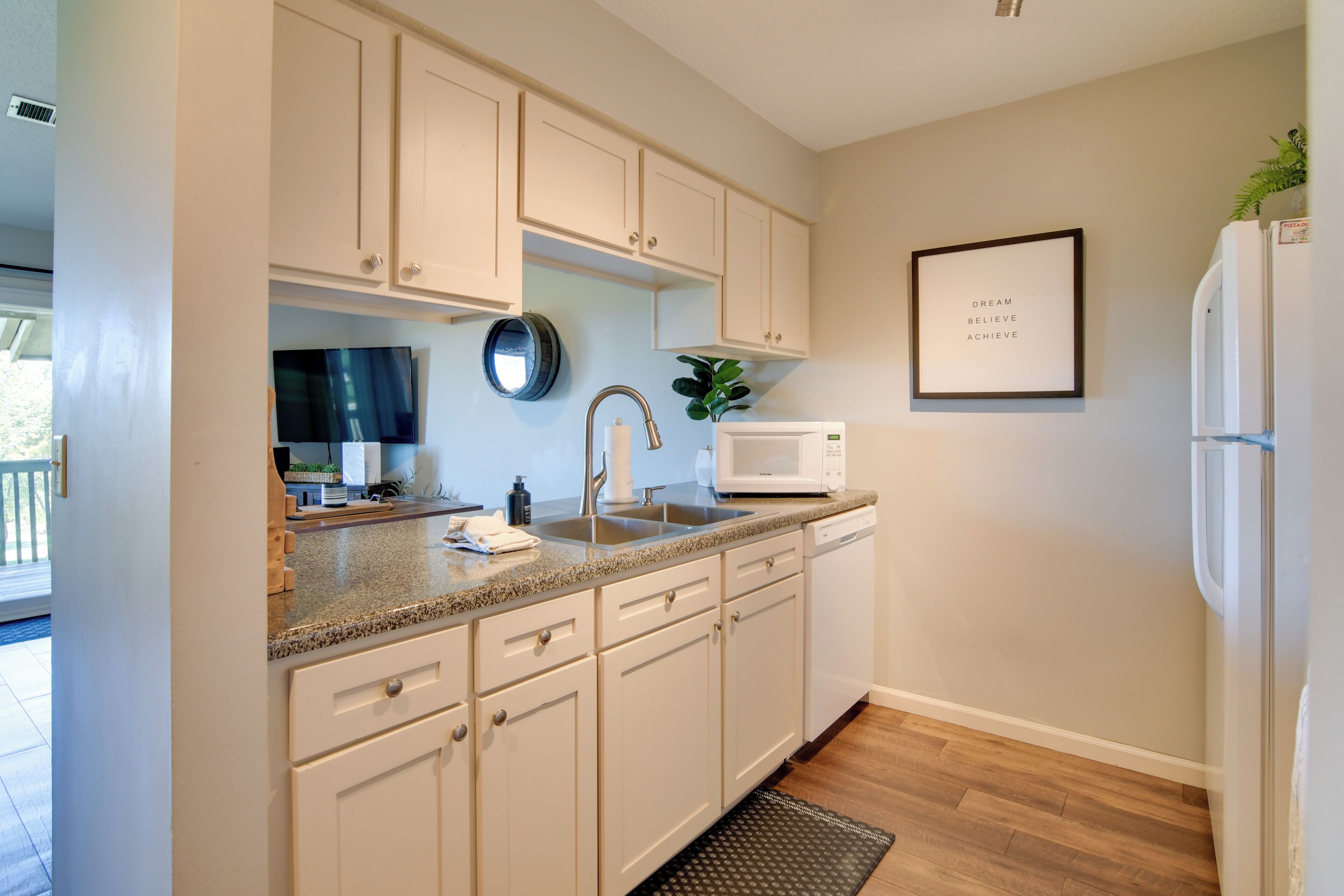A kitchen with white cabinets, a microwave, a sink, and a framed inspirational quote on the wall.