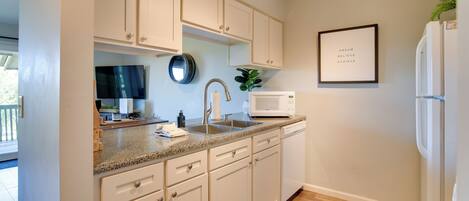 A kitchen with white cabinets, a microwave, a sink, and a framed inspirational quote on the wall.