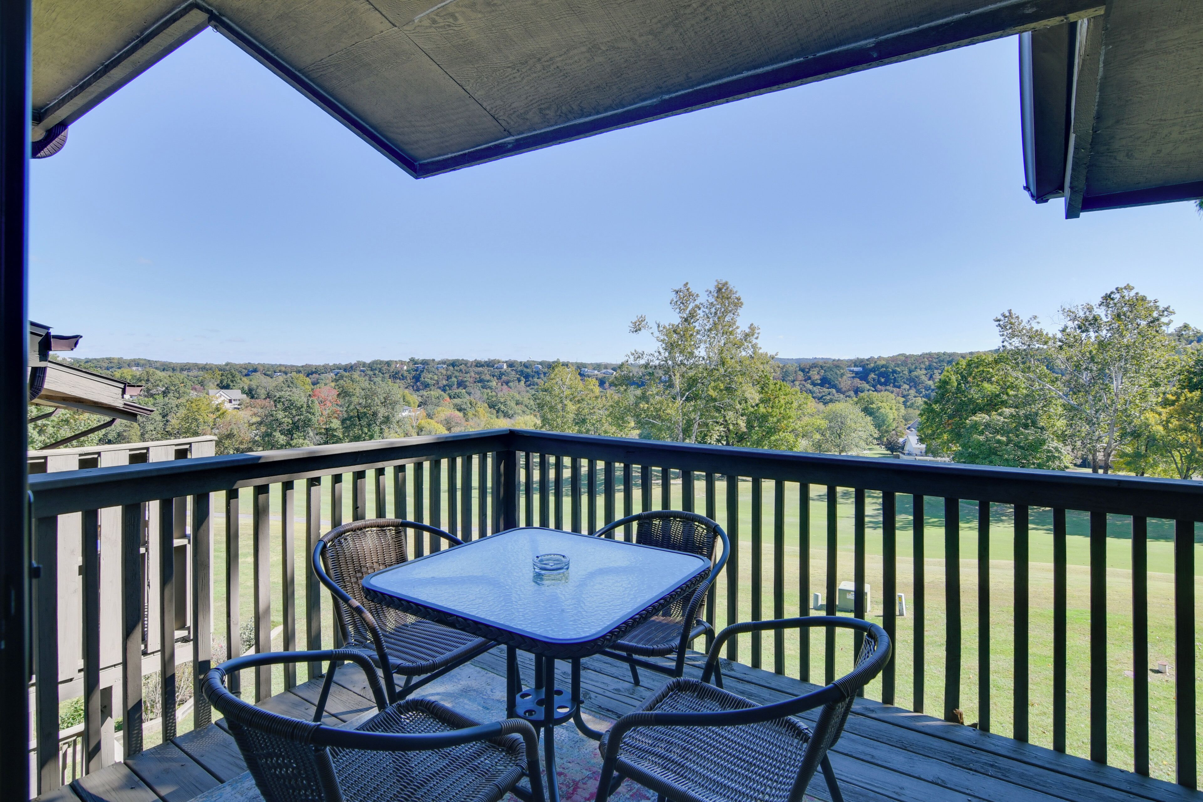Un balcon avec une table et des chaises, donnant sur un paysage verdoyant, avec des arbres et des collines.