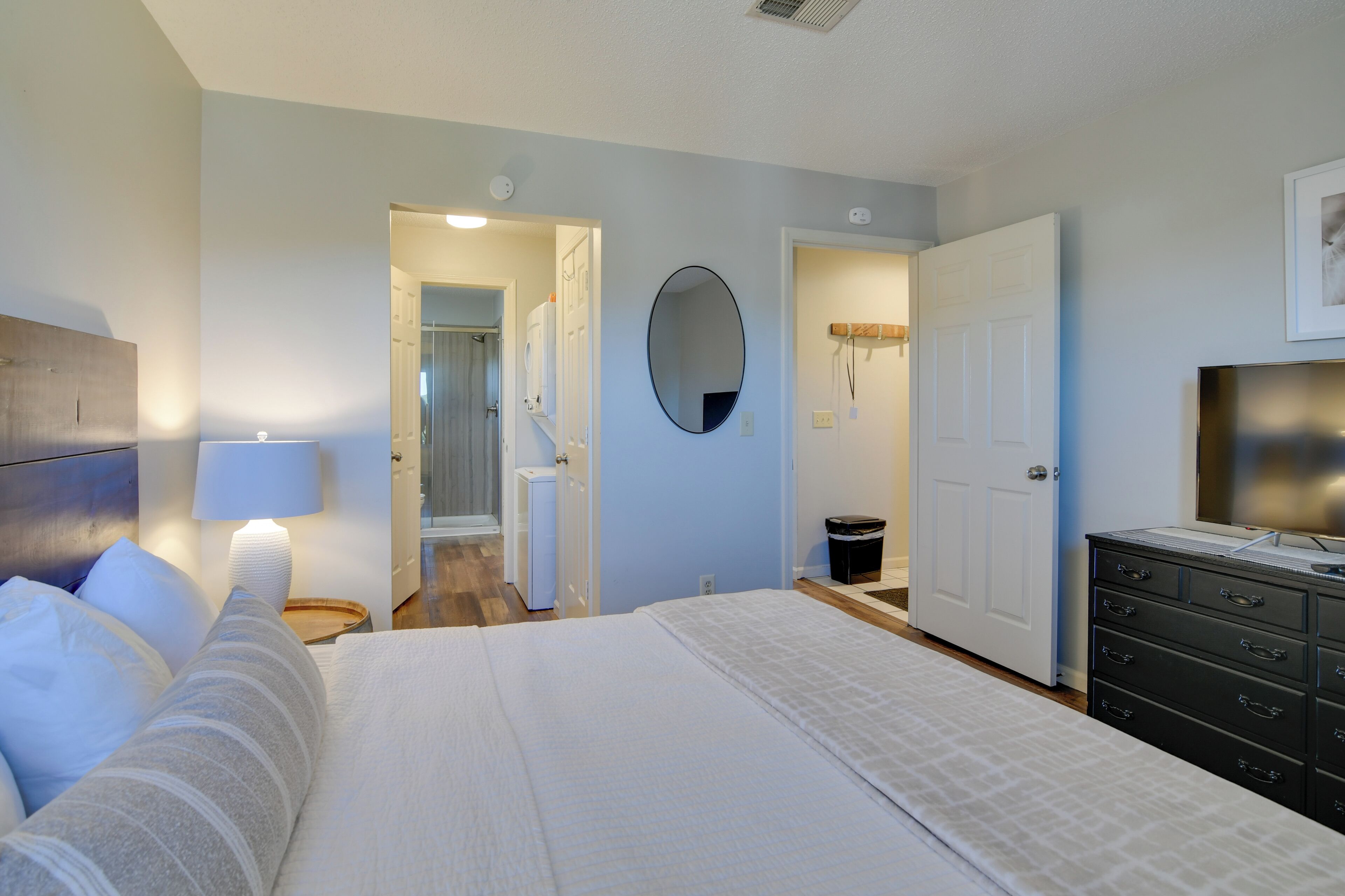 A bedroom with a bed, a dresser, a mirror, and a door leading to a bathroom.
