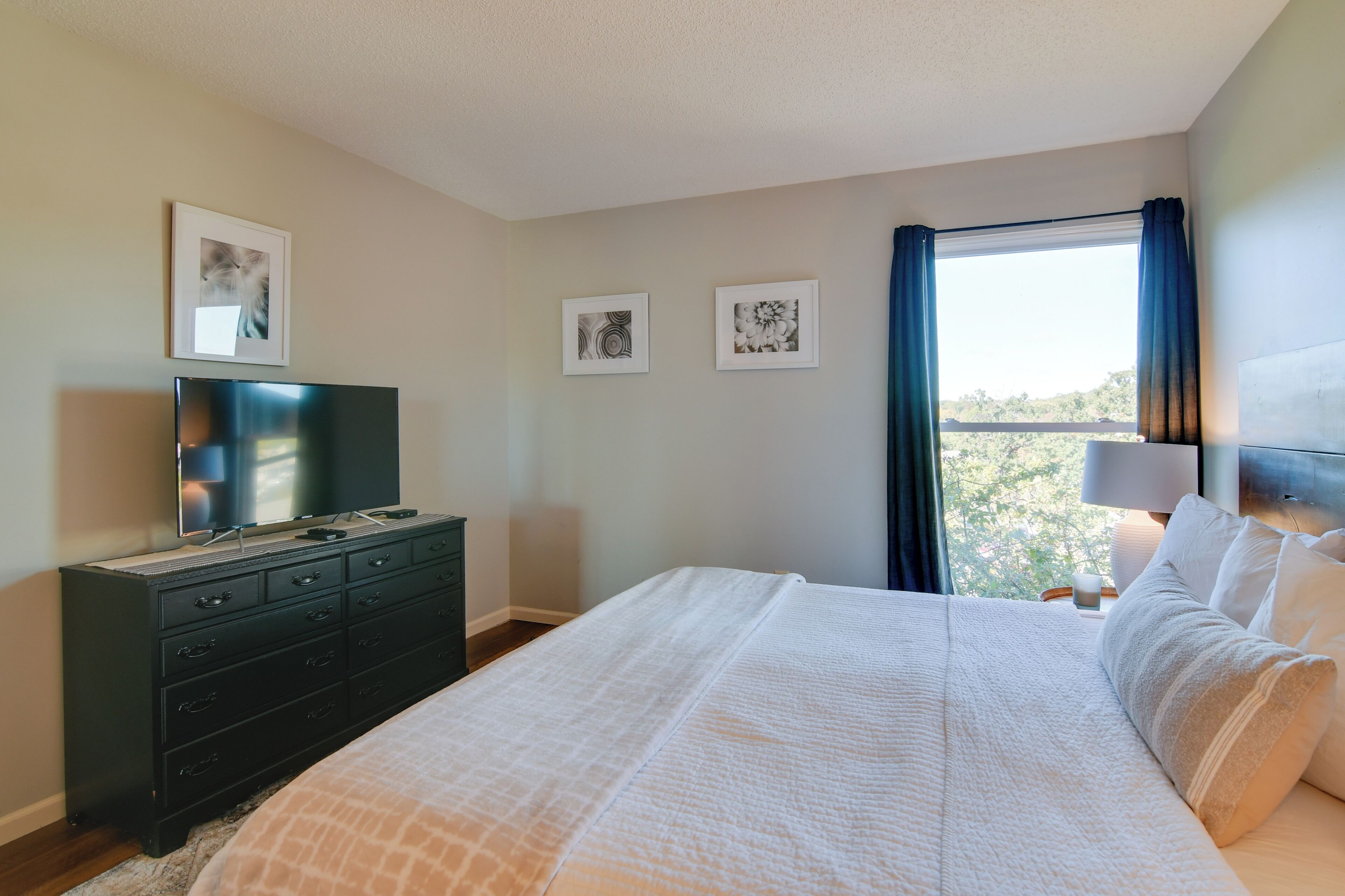Une chambre à coucher avec un lit, une commode, un téléviseur et des tableaux encadrés accrochés au mur.