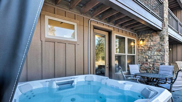 A hot tub with a stone wall and wooden paneling, outdoor furniture, and a view of the surrounding area.