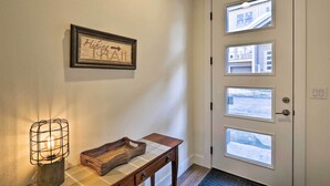 A hallway with a framed sign reading "Hiking Trail," a table with a basket, and a door with multiple windows.