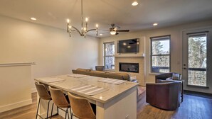 A modern kitchen with a central island, bar stools, a fireplace, and large windows.