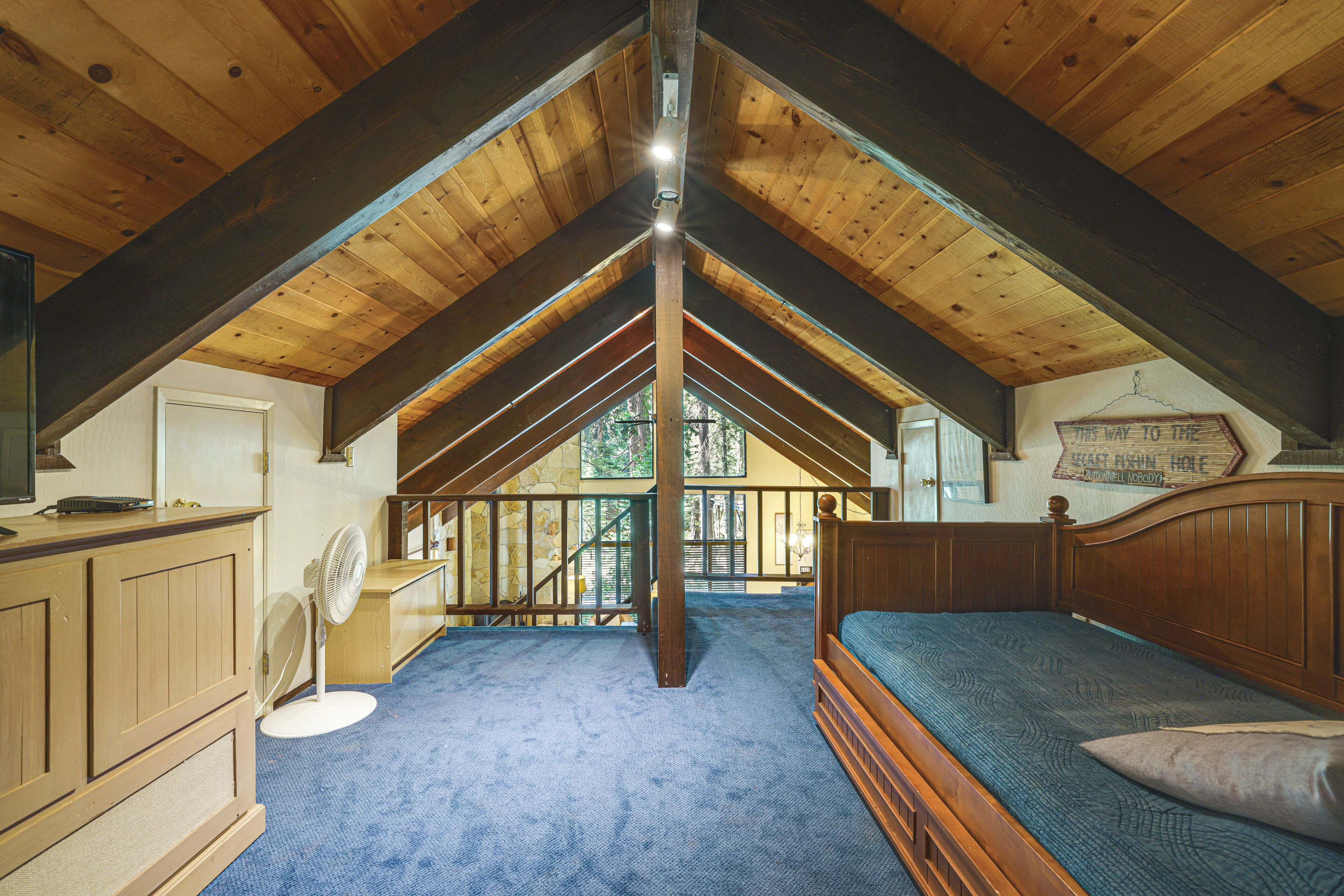 A bedroom with a wooden ceiling, a bed, a desk with a chair, and a fan.