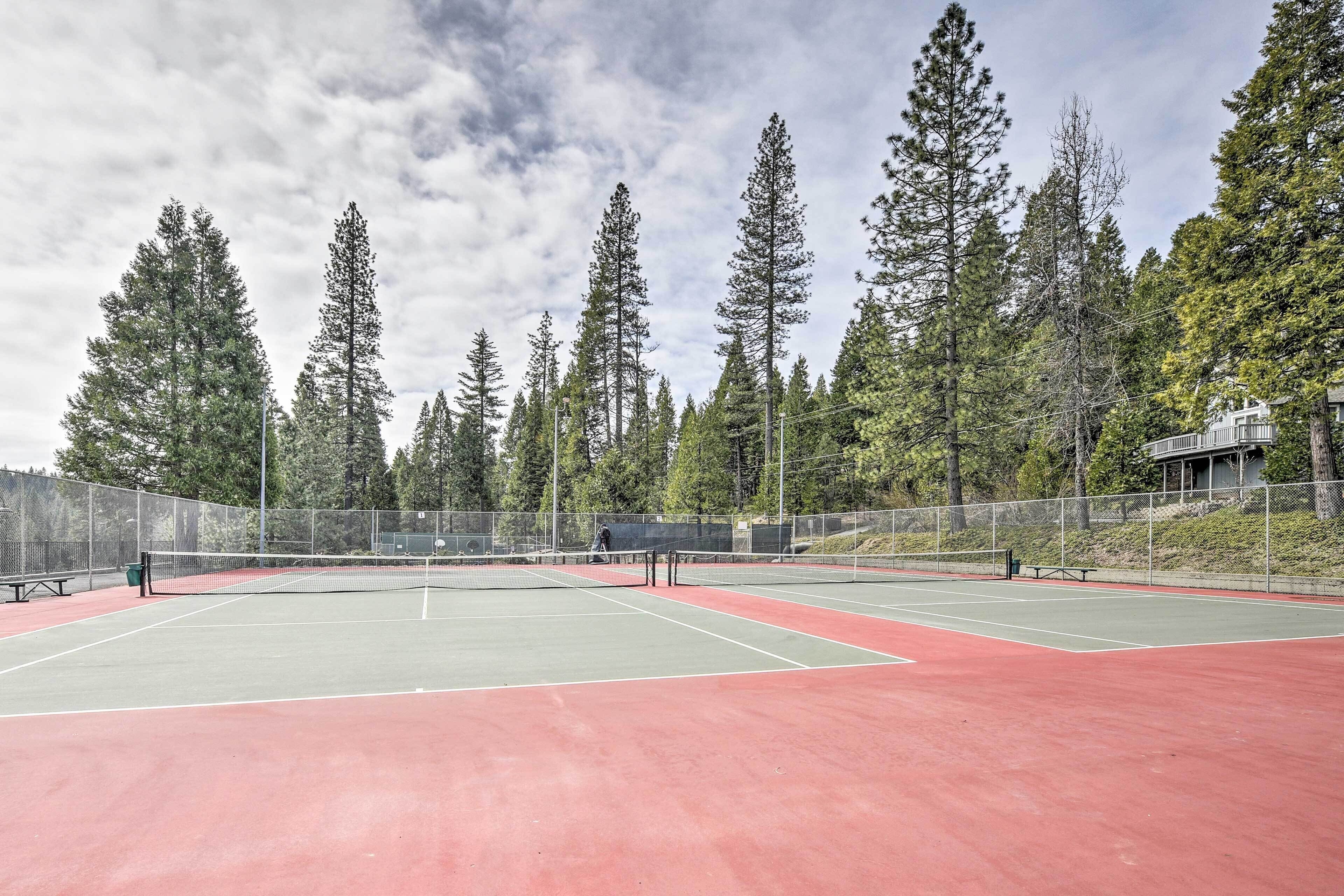 An outdoor tennis court surrounded by tall trees and a building in the background.