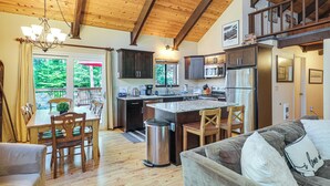 Une cuisine spacieuse avec des poutres en bois, un coin repas avec une table et des chaises, et un salon avec un canapé et des coussins.