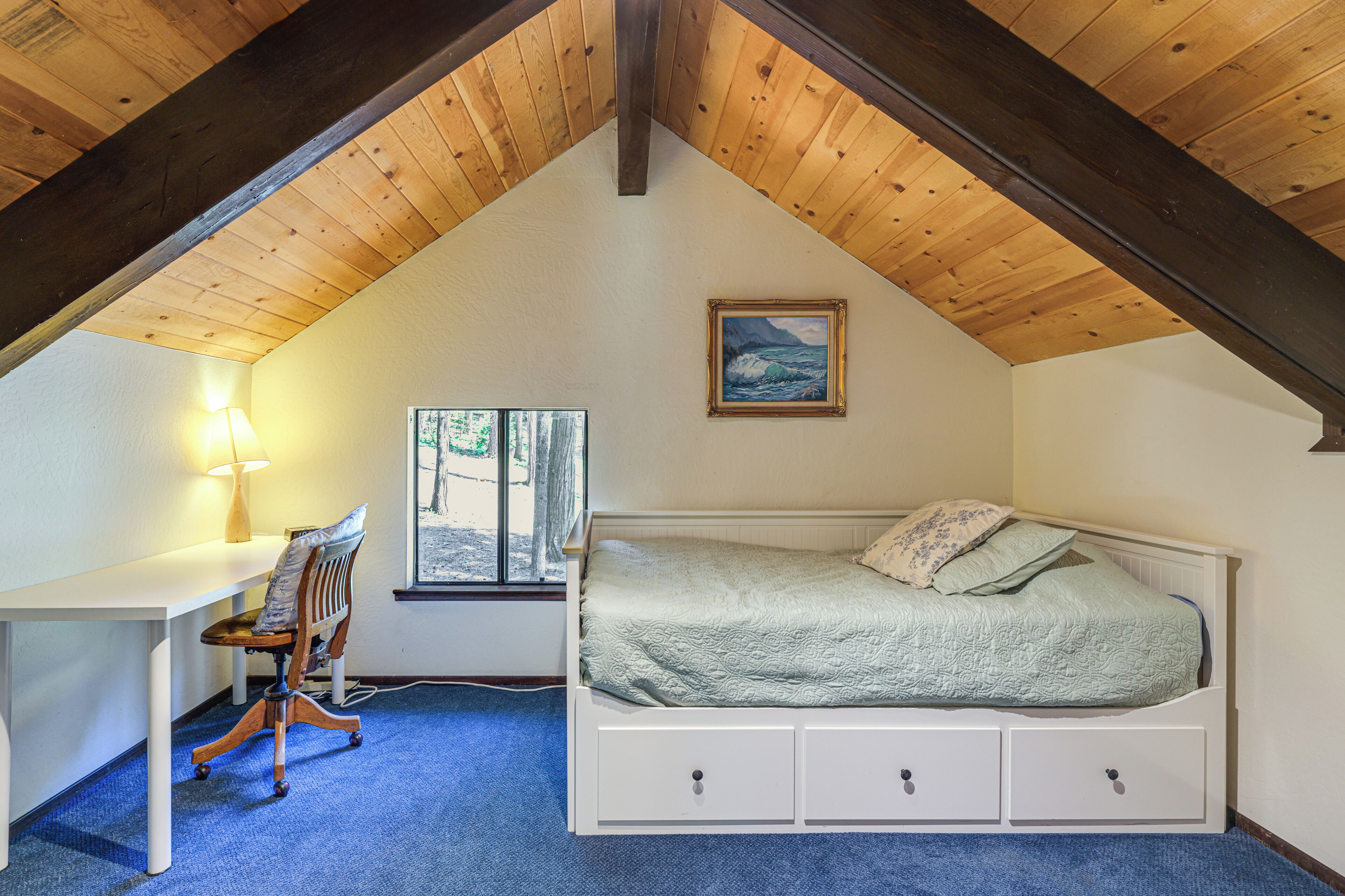 A bedroom with a sloped ceiling, a bed, a desk, and a chair.
