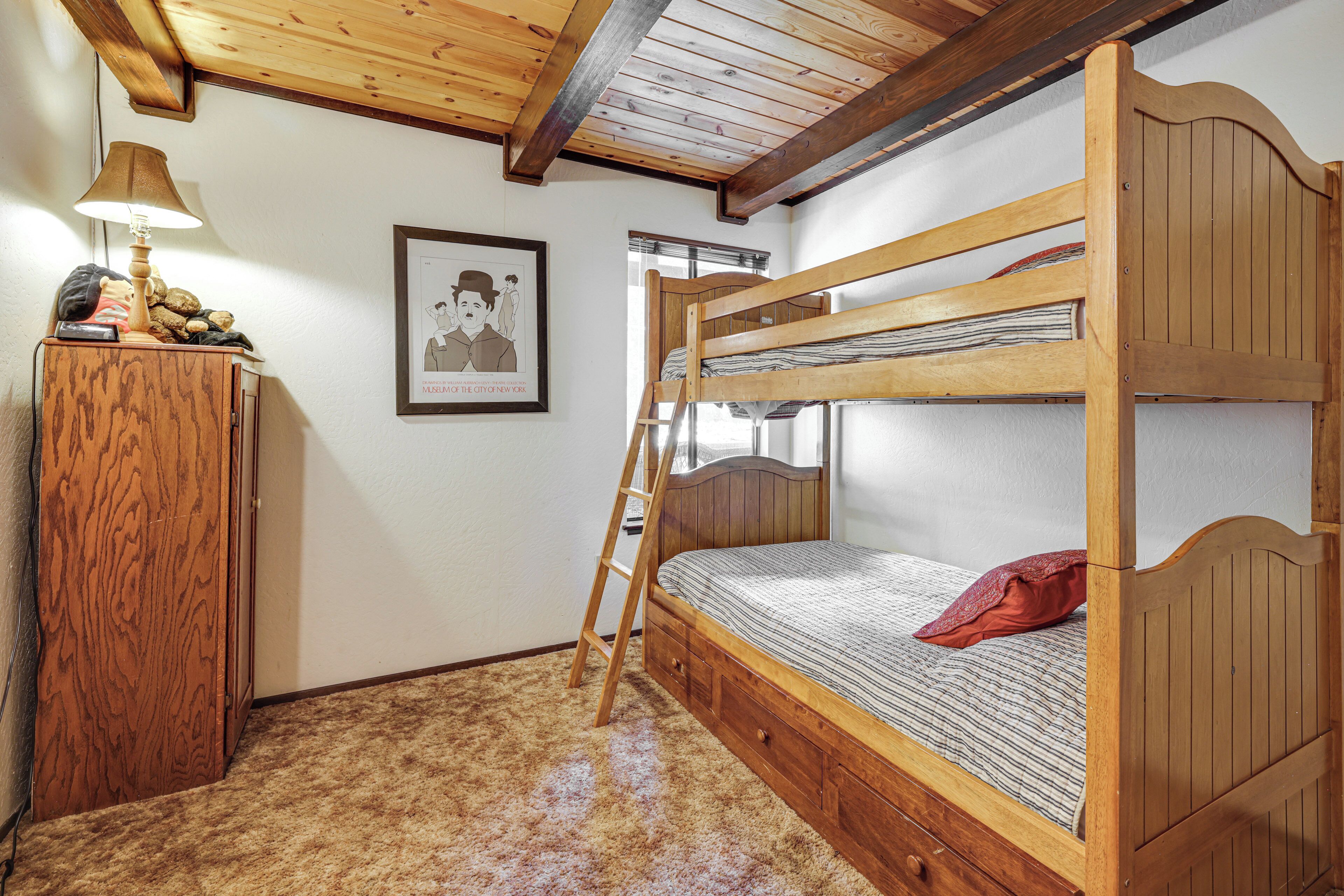 Ein Etagenbett mit Holzkopfstück, ein Holzkleiderschrank, ein gerahmtes Bild an der Wand und eine an der Wand angelehnte Leiter.