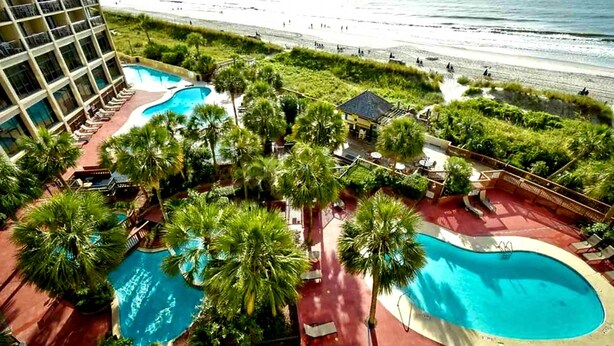 Ein Resort mit mehreren Schwimmbecken, umgeben von Palmen und Blick auf einen Strand.